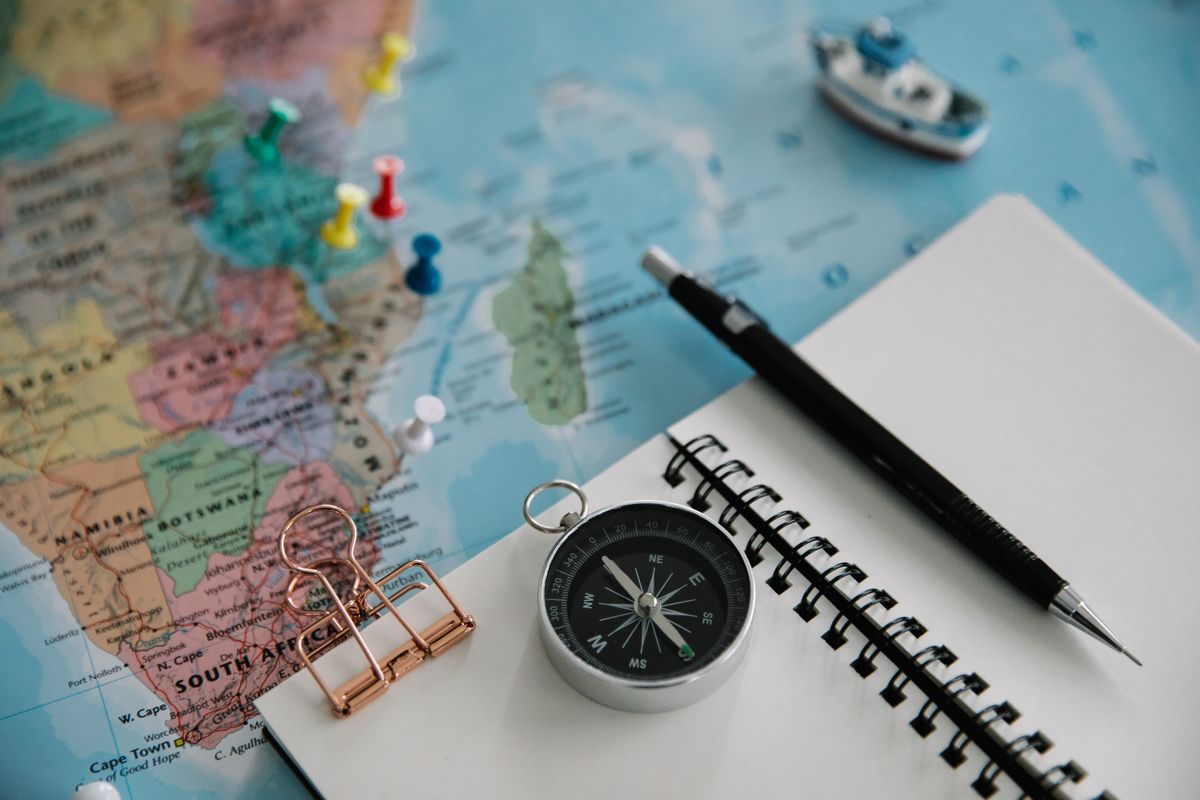Travel planning flat lay: world map with pins, compass, notebook and pen