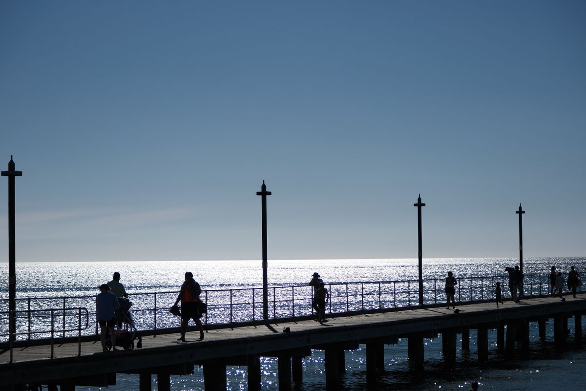 Silhouetted people strolling along a pier above sparkling water