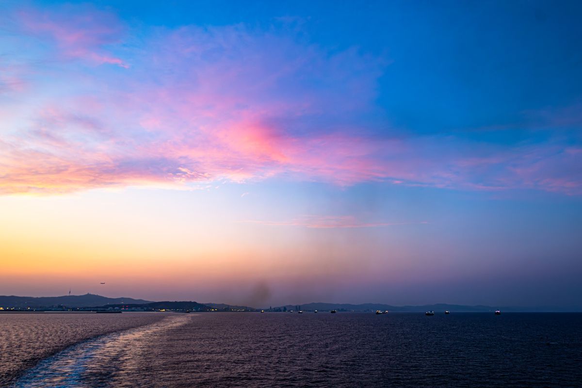 Pink and blue sunset sky over calm sea, seen from a ship with its wake below