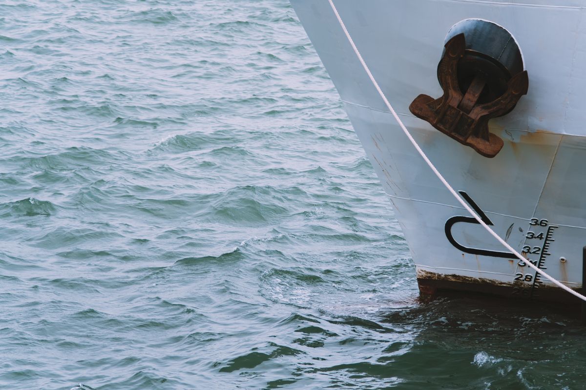 Bow of a ship with its anchor above gently rolling blue-green water